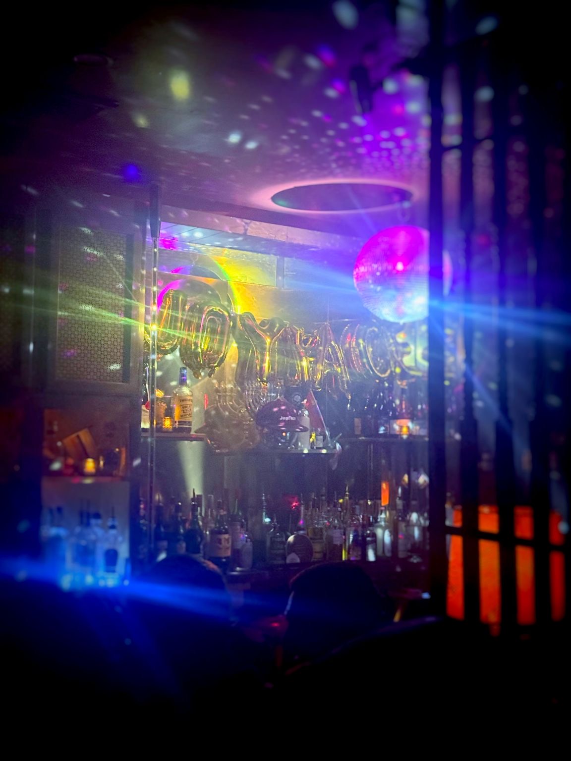 A bar lit by a disco ball, with gold balloon letters over the shelves